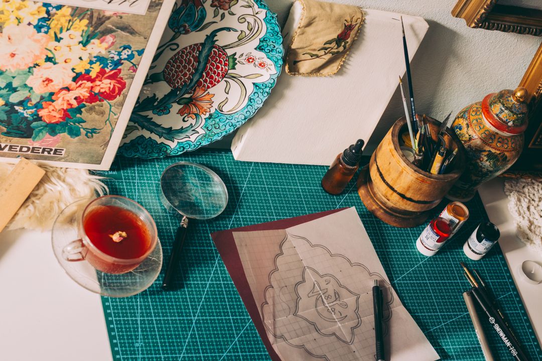 Overhead view of an artistic workspace with sketches, brushes, tea, and creative tools.