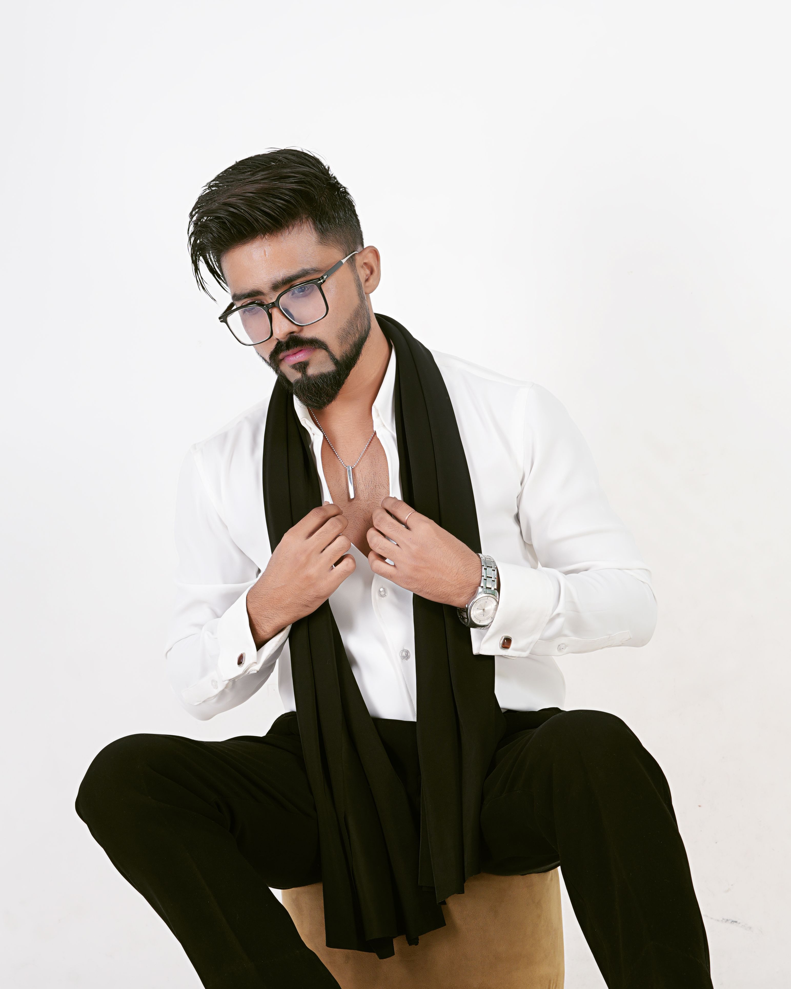 A fashionable young man wearing a white shirt and black scarf, sitting confidently.