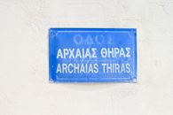 A vibrant blue street sign with Greek and English text, symbolizing Ancient Thira in Fira, Greece.