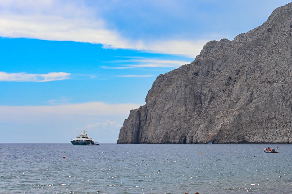 Breathtaking Kissamos Balos Lagoon Sunset Catamaran Cruise Review: Sailing Crete's Most Stunning Lagoon at Golden Hour Review 2026 - A picturesque view of a yacht near towering cliffs on a sunny day in Fira, Greece.