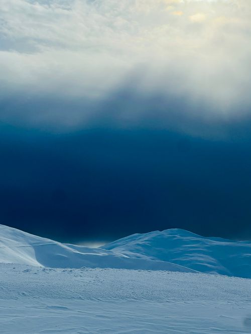 Free Beautiful snow-covered mountain landscape with dramatic sky and sunlight rays at dawn, creating a serene winter atmosphere. Stock Photo