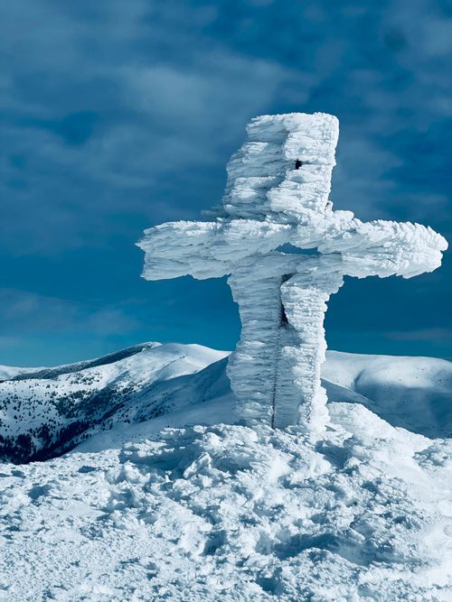Free A serene icy cross stands majestically atop a snow-covered mountain in winter. Stock Photo