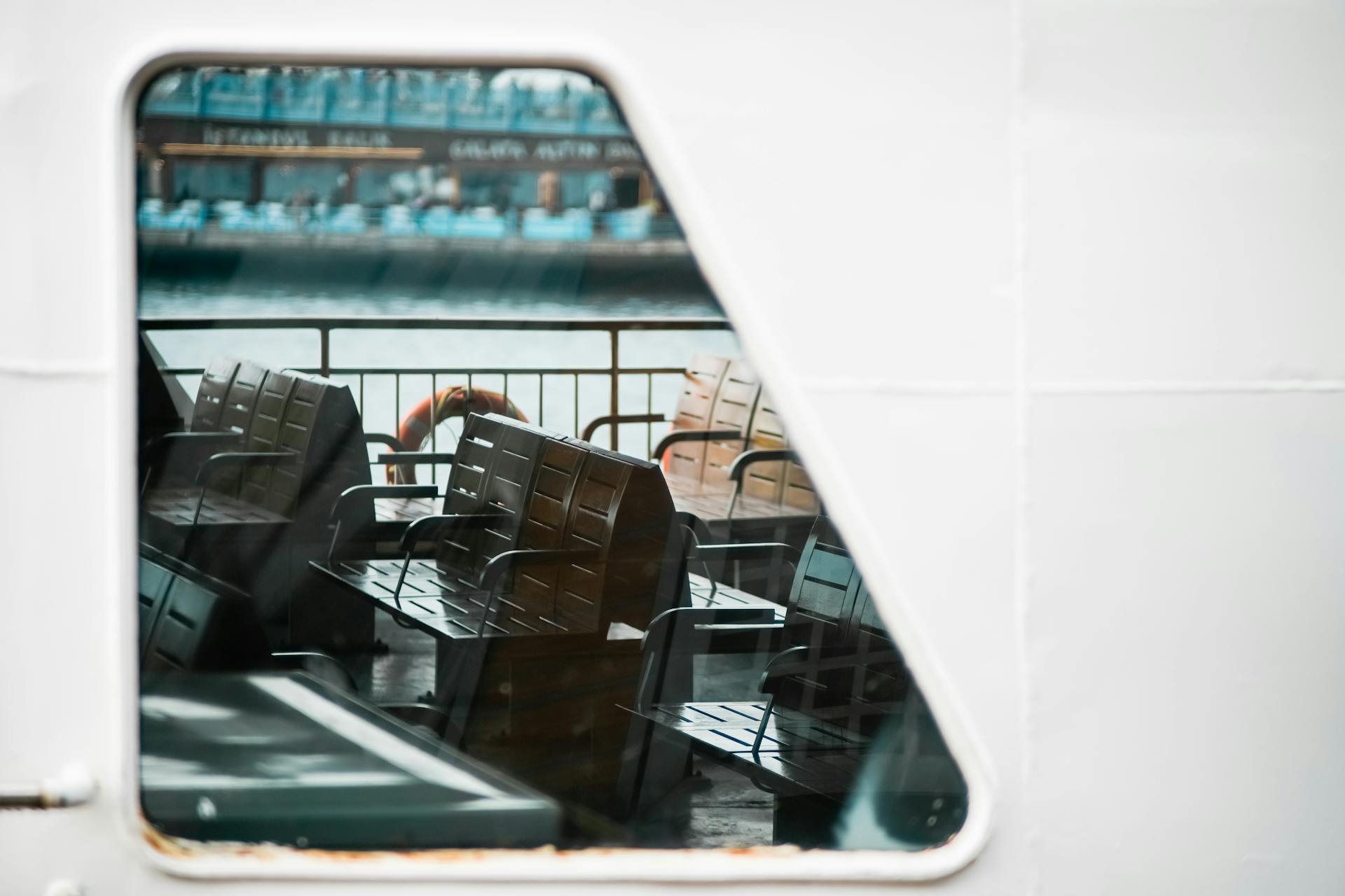 Reflection of empty seats through a window on a ship with blurred water outside.