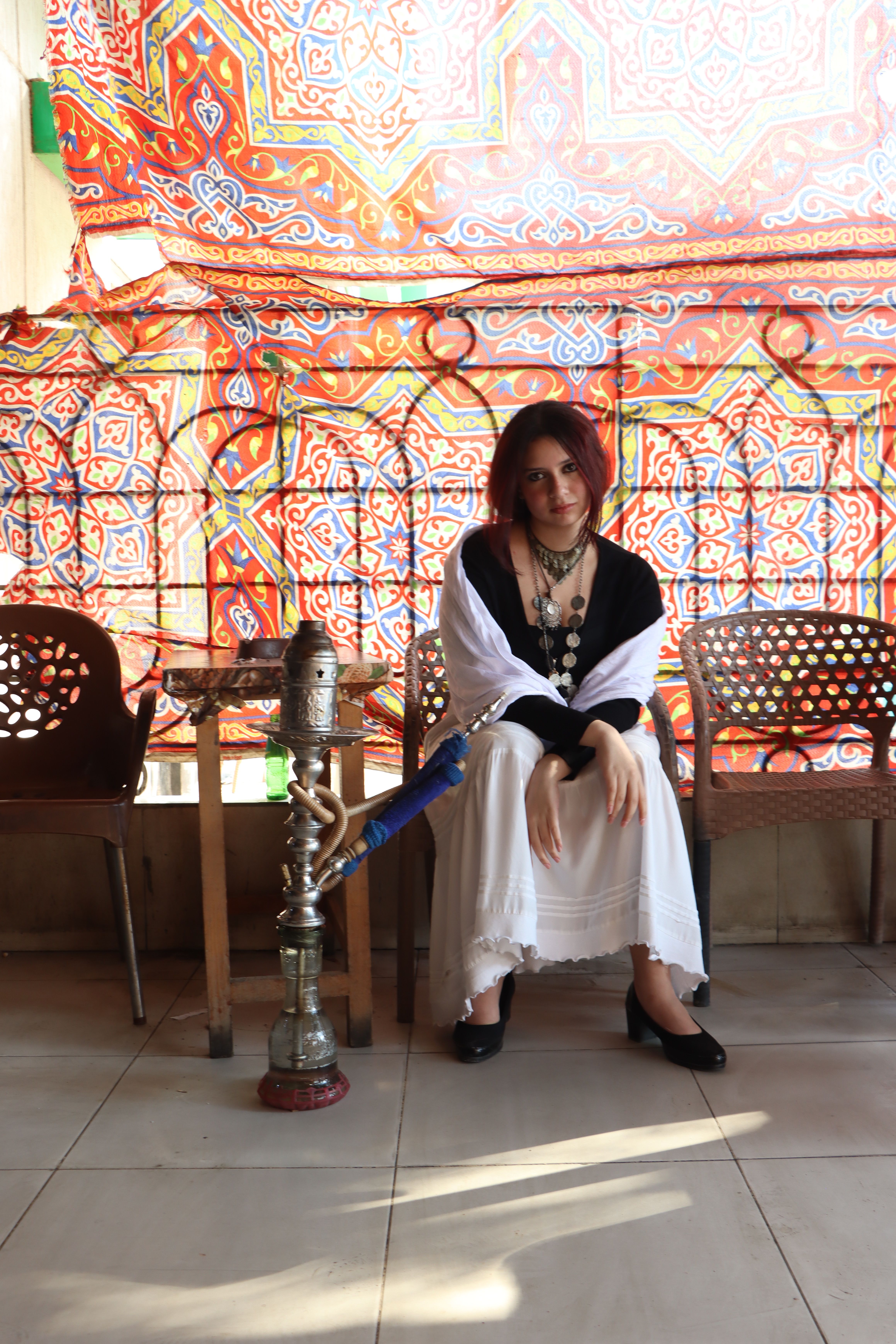 Elegantly dressed woman enjoying a hookah in a vibrant Cairo cafe setting with colorful patterns.