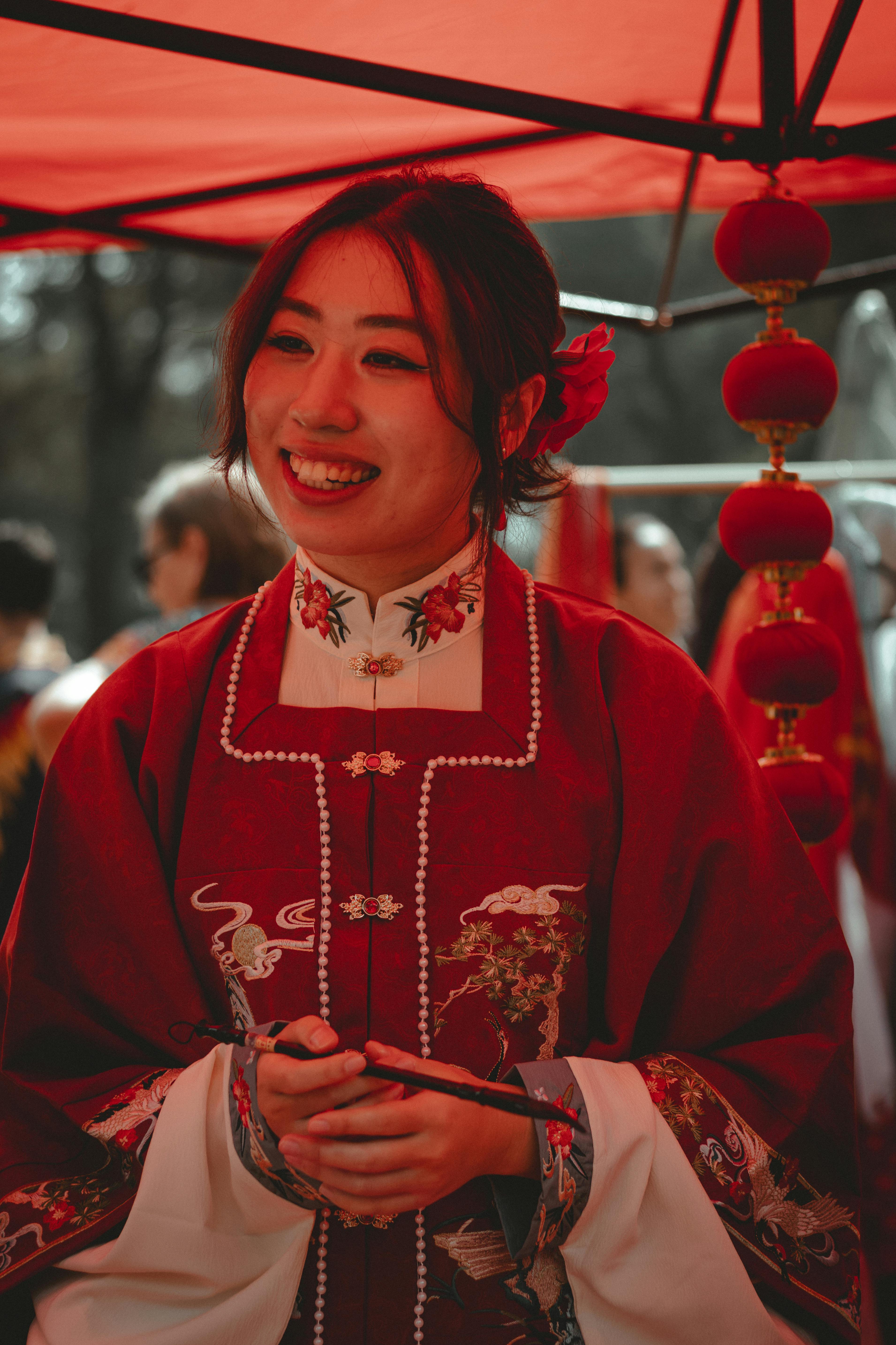 A woman wearing a traditional red costume smiles under a red tent during a city festival.