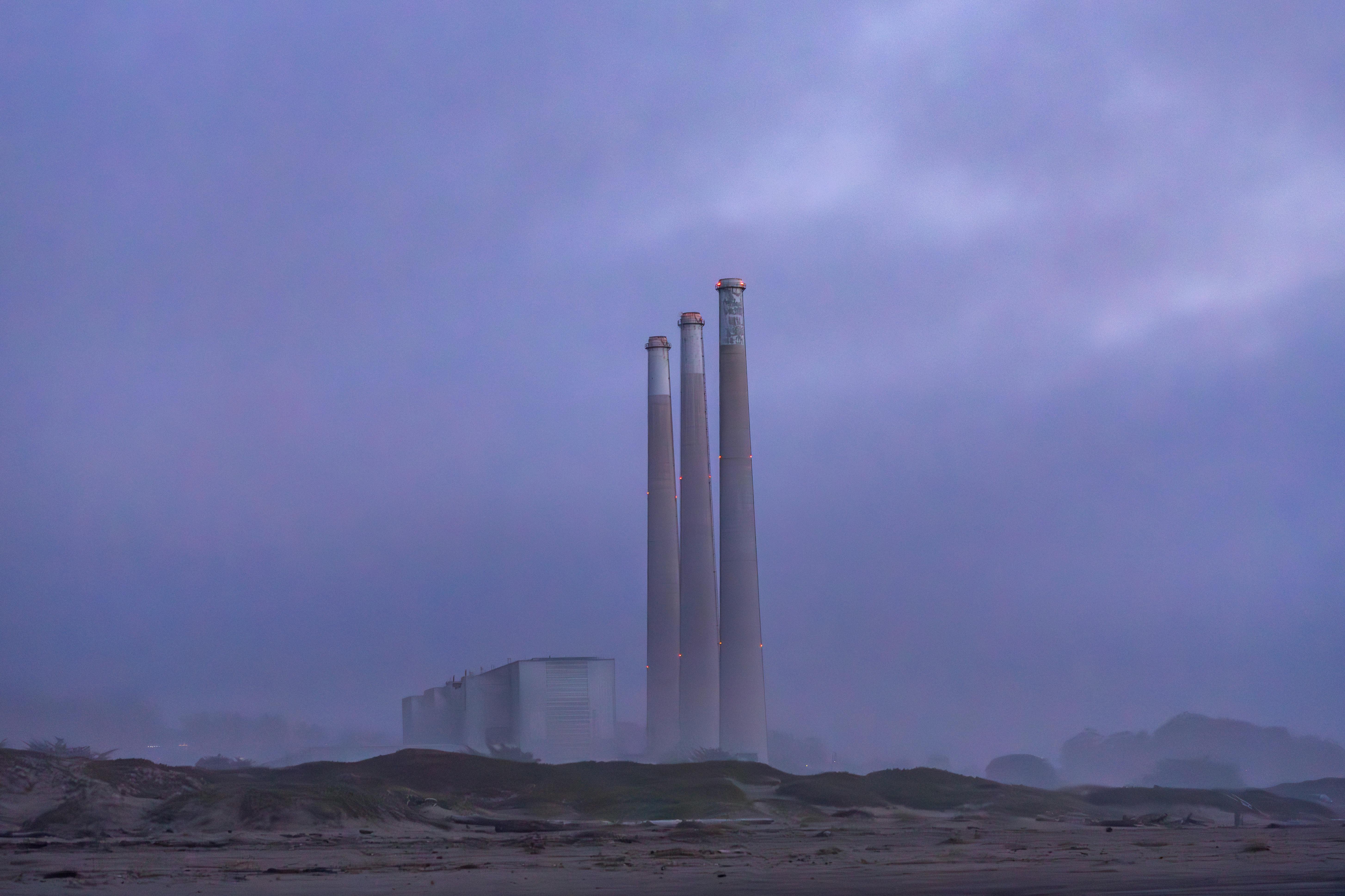 Misty three smokestacks of a power plant at dawn create a serene industrial scene.