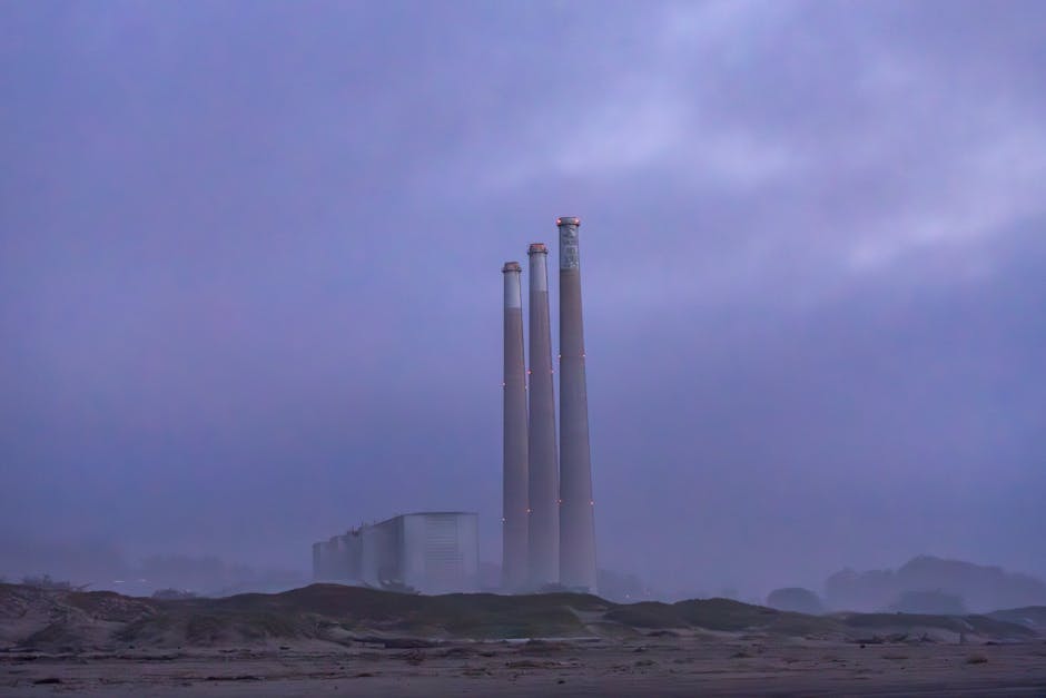 Misty three smokestacks of a power plant at dawn create a serene industrial scene.