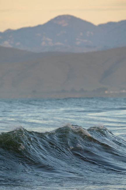 Peaceful ocean waves against a mountain background captured at sunset.