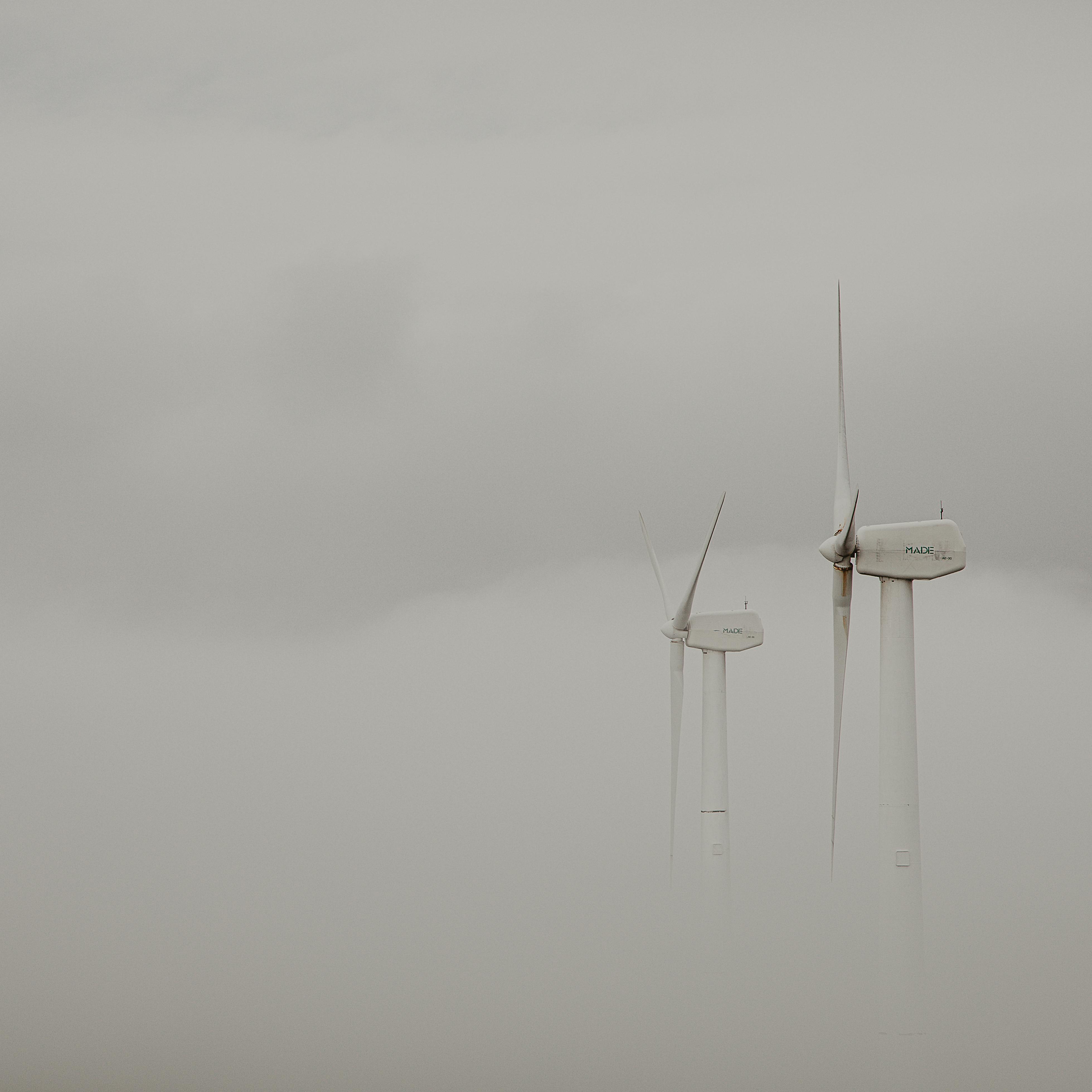 Wind turbines emerging through dense fog in Galicia, creating an ethereal landscape.