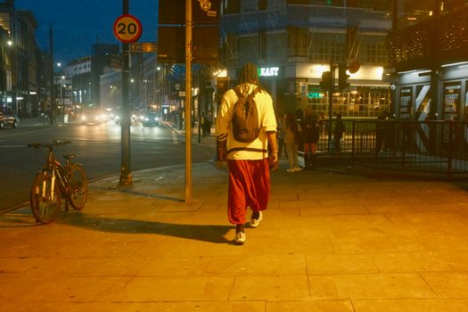 Man walking down a London street at night with a backpack, capturing city life.