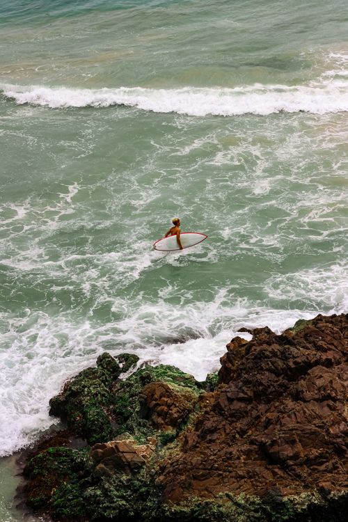 Free A lone surfer treks into the waves in Byron Bay, Australia, showcasing the rugged coastline. Stock Photo