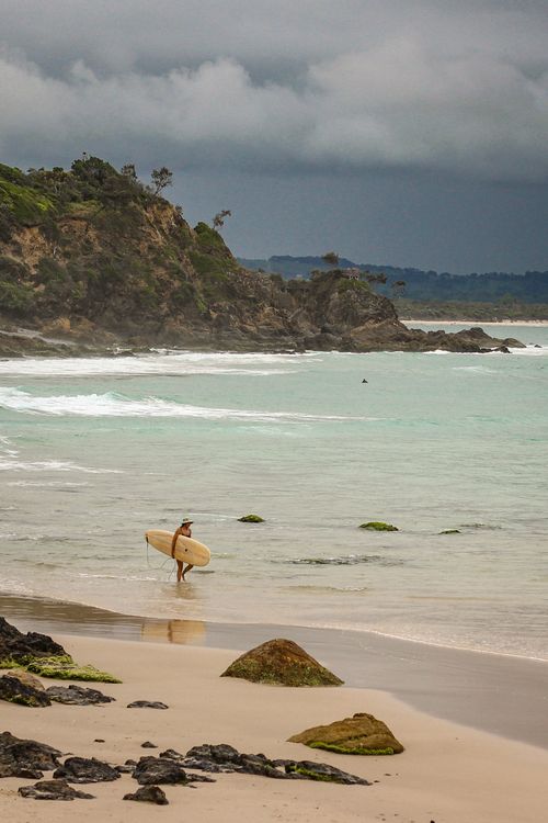Free A lone surfer walking on Byron Bay beach under cloudy skies, showcasing Australia's coastal beauty. Stock Photo