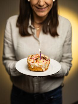 A woman holding a donut with a lit candle, ideal for birthdays and celebrations.
