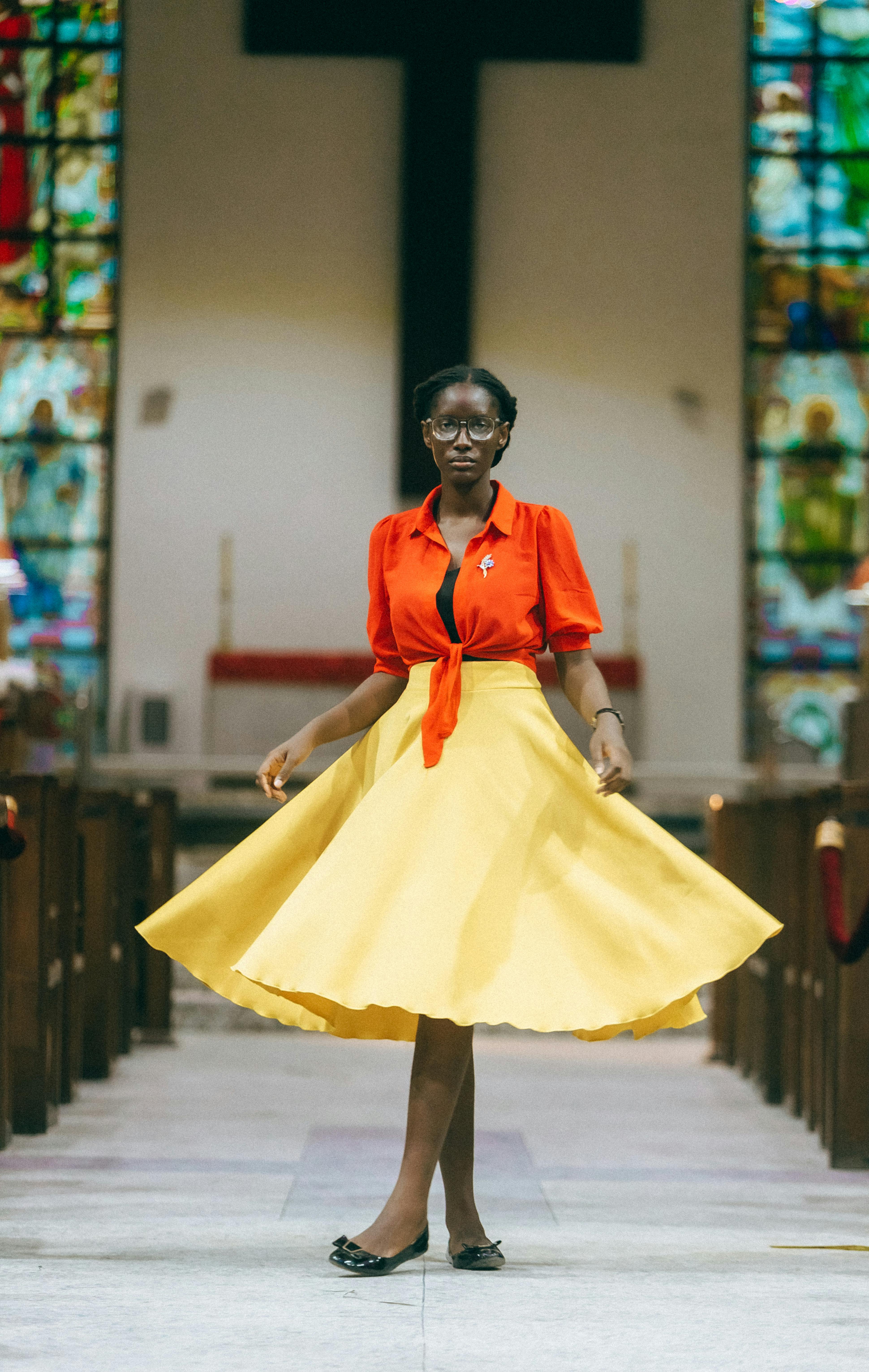 Gratis Model Afrika yang bergaya dengan gaun cerah, berpose di gereja dengan latar belakang kaca patri. Foto Stok