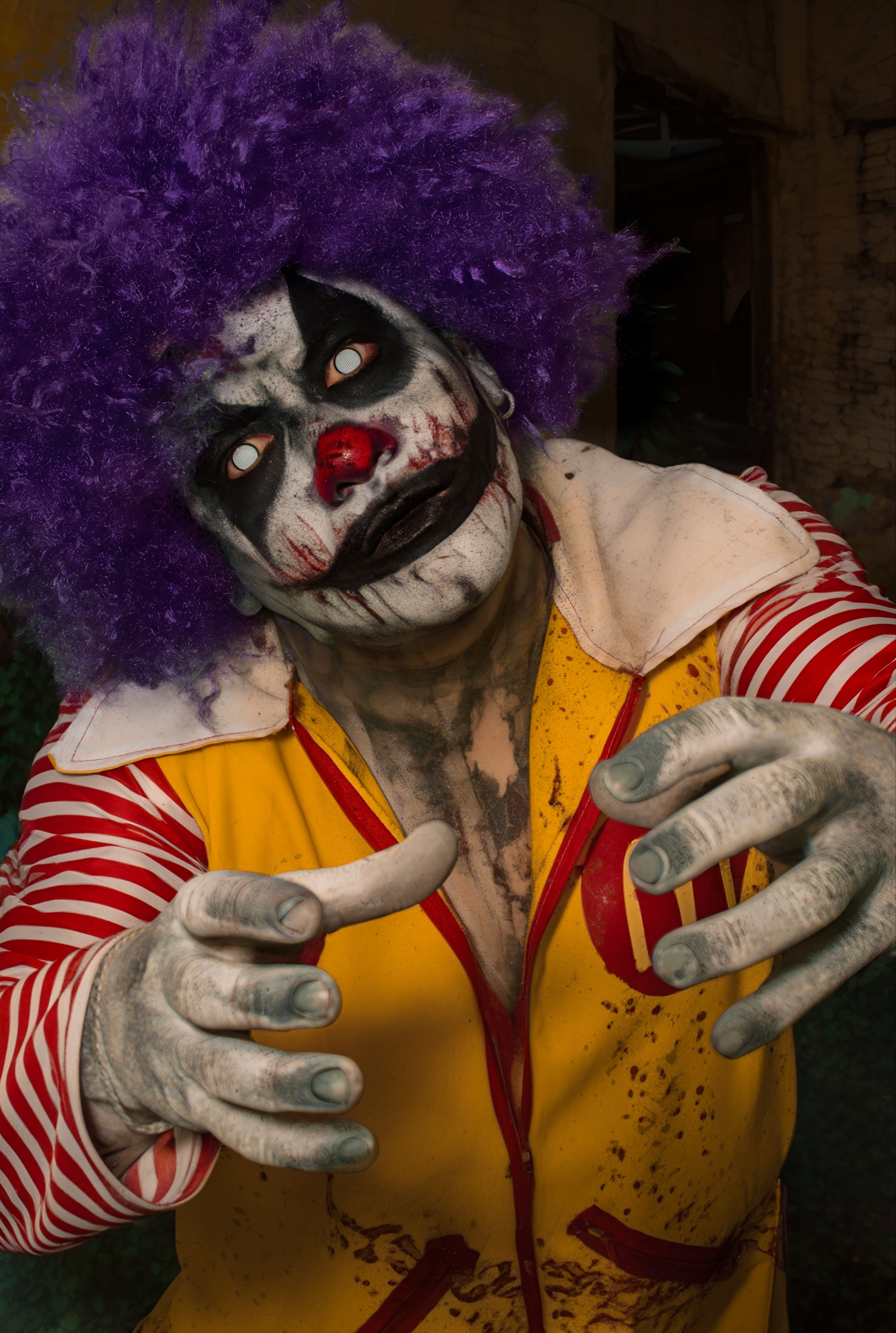 Creepy clown with makeup and colorful costume reaching out in dark atmosphere.