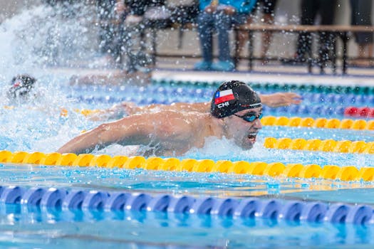 Male swimmer performing butterfly stroke in a competitive indoor pool race.