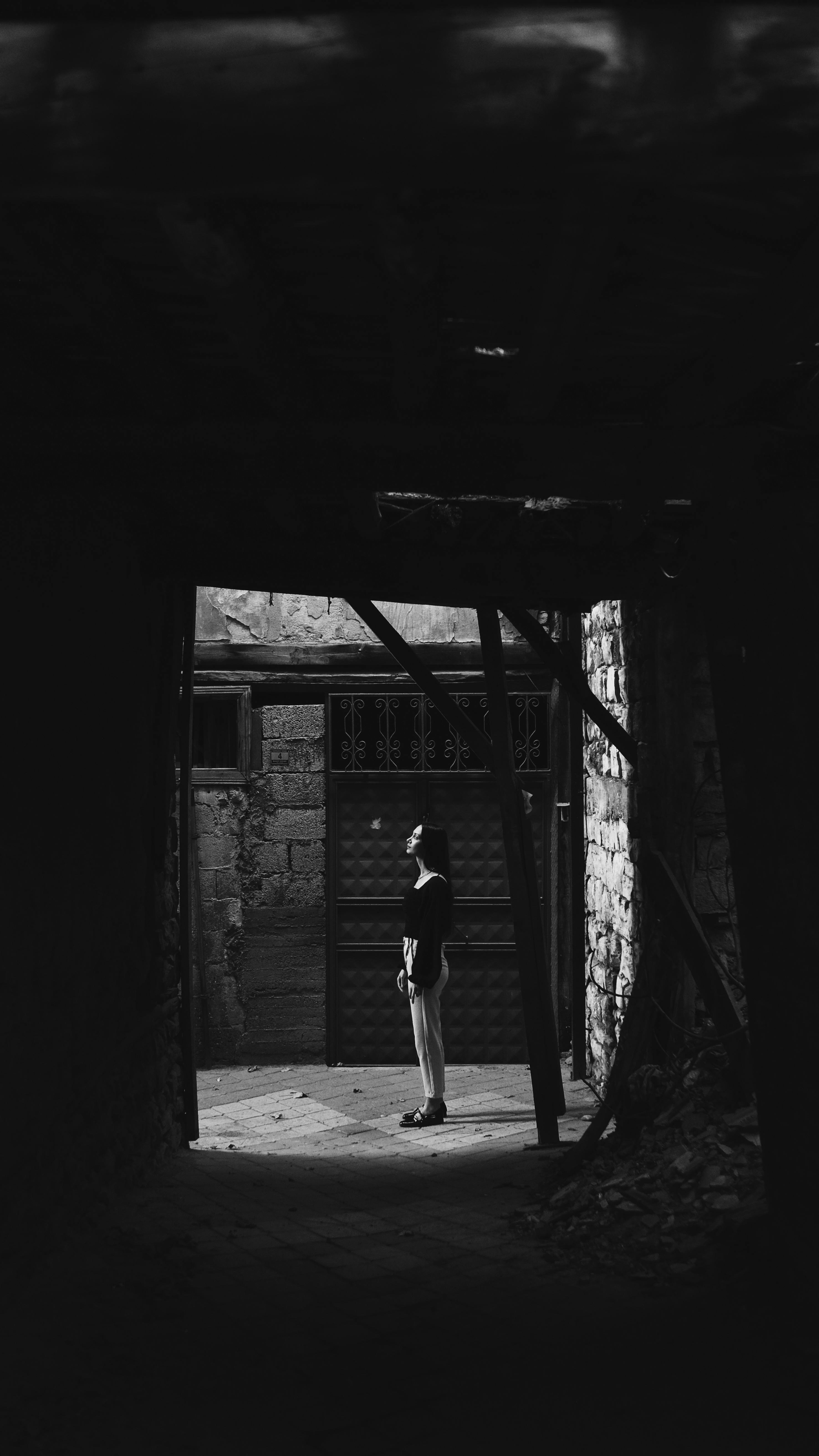 A solitary figure stands in a dramatic black and white alleyway scene, evoking a sense of mystery.