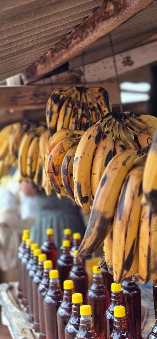 Free Cluster of ripe bananas hanging in a rustic market with honey bottles below. Stock Photo
