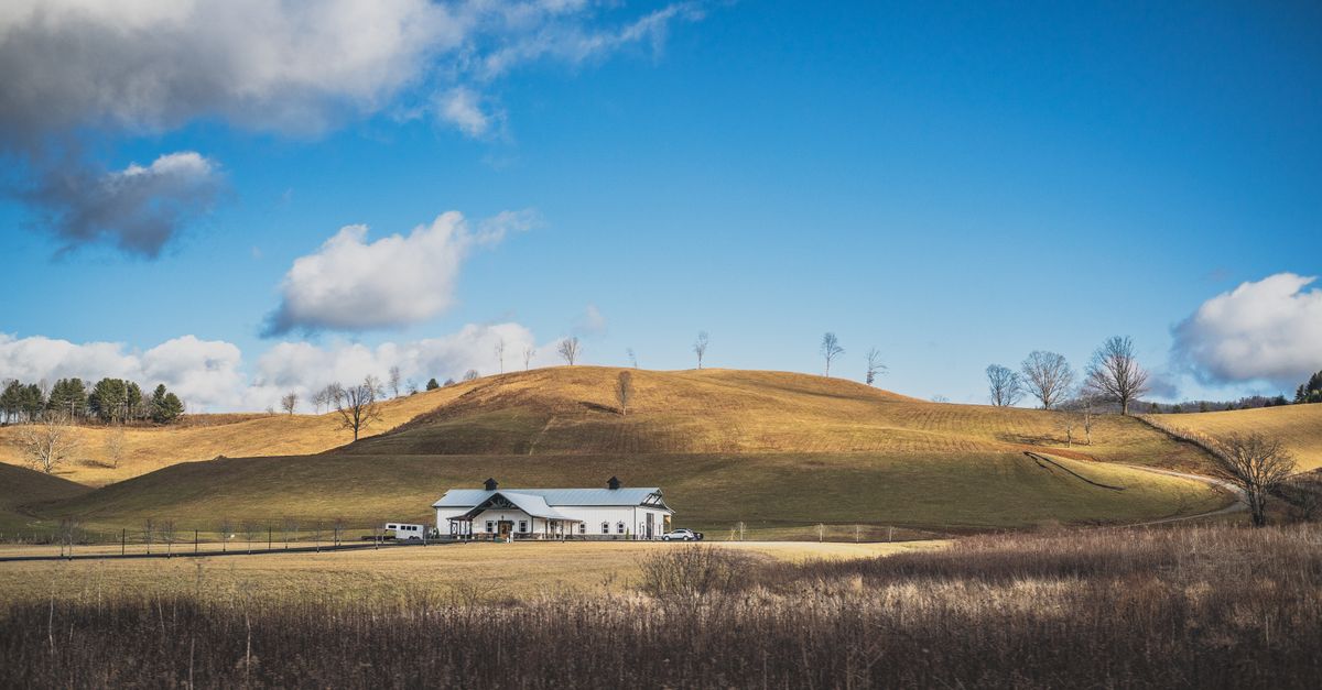 Charming farmhouse nestled in scenic rolling hills under a bright sky.