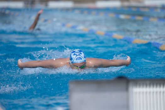 Swimmer in action executing butterfly stroke in a pool during a day swim meet.