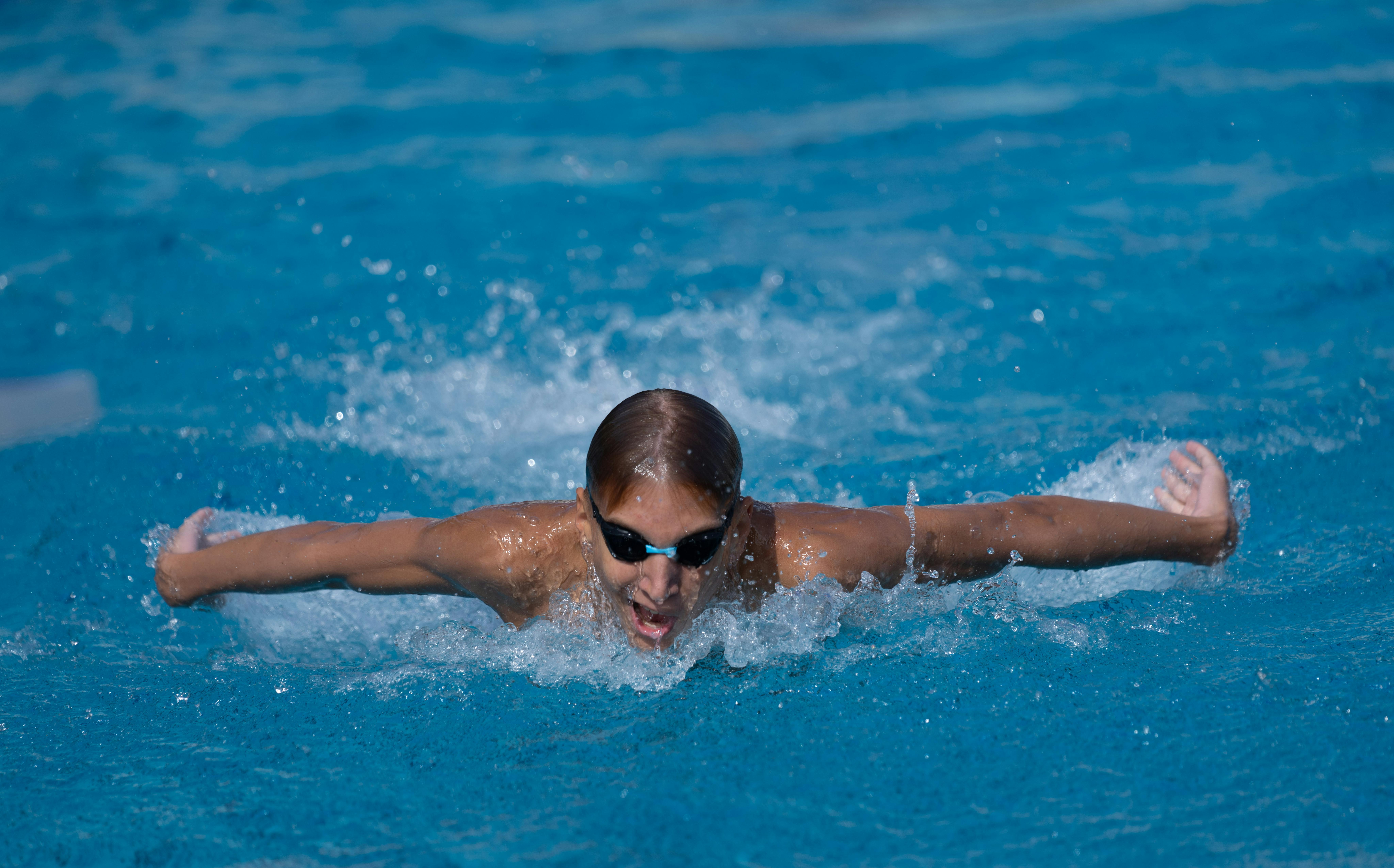 Energetic young athlete swimming butterfly stroke in a bright outdoor pool.