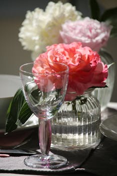 Beautiful table setting with a wine glass and colorful peonies in vases, creating an elegant ambiance.