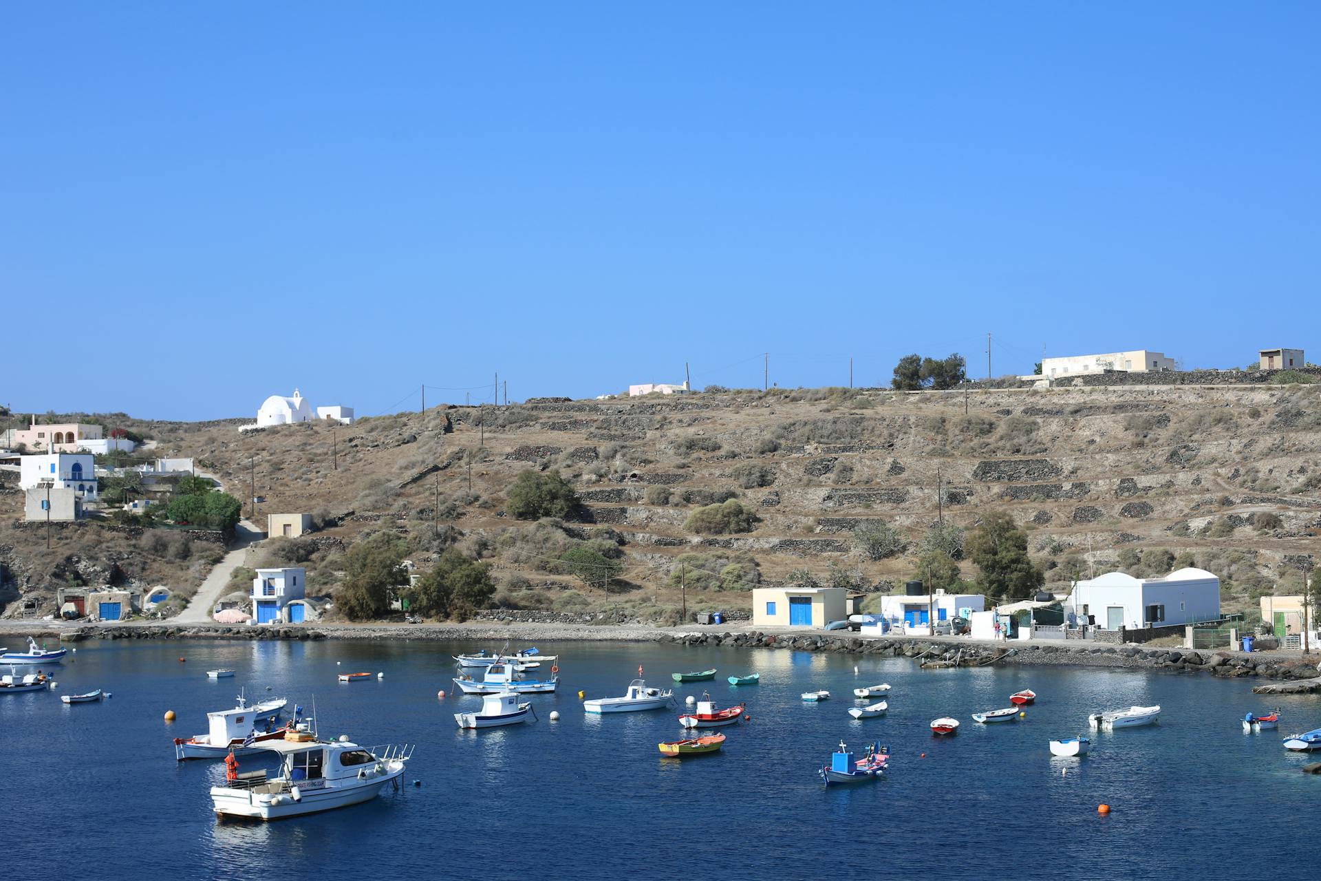 Picturesque harbor with boats and traditional buildings on a Greek island under blue sky.