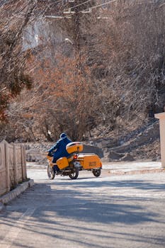 A person rides a yellow motorcycle with a sidecar on a chilly winter street, surrounded by bare trees.