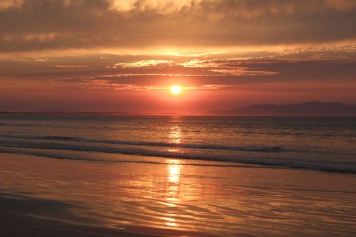 Free Tranquil sunset over ocean waves, reflecting warm hues across the sandy beach. Stock Photo
