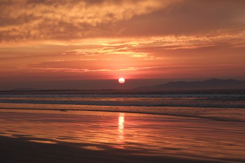 Free A serene beach sunset with golden skies and reflected water, creating a peaceful ambiance. Stock Photo
