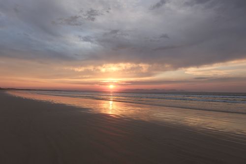 Free A tranquil beach sunset with a colorful sky reflecting on the smooth sand, creating a peaceful atmosphere. Stock Photo