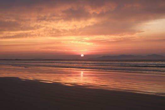 Peaceful sunset over a calm beach with gentle waves and warm glowing sky.