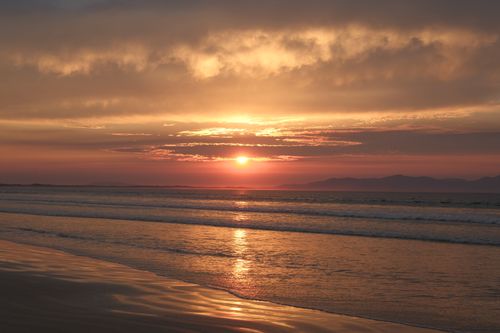 Free Captivating sunset over a tranquil beach with gentle waves and vibrant sky. Stock Photo