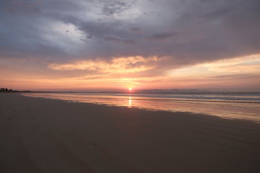 A tranquil beach at sunrise with stunning clouds and soft wave reflections.