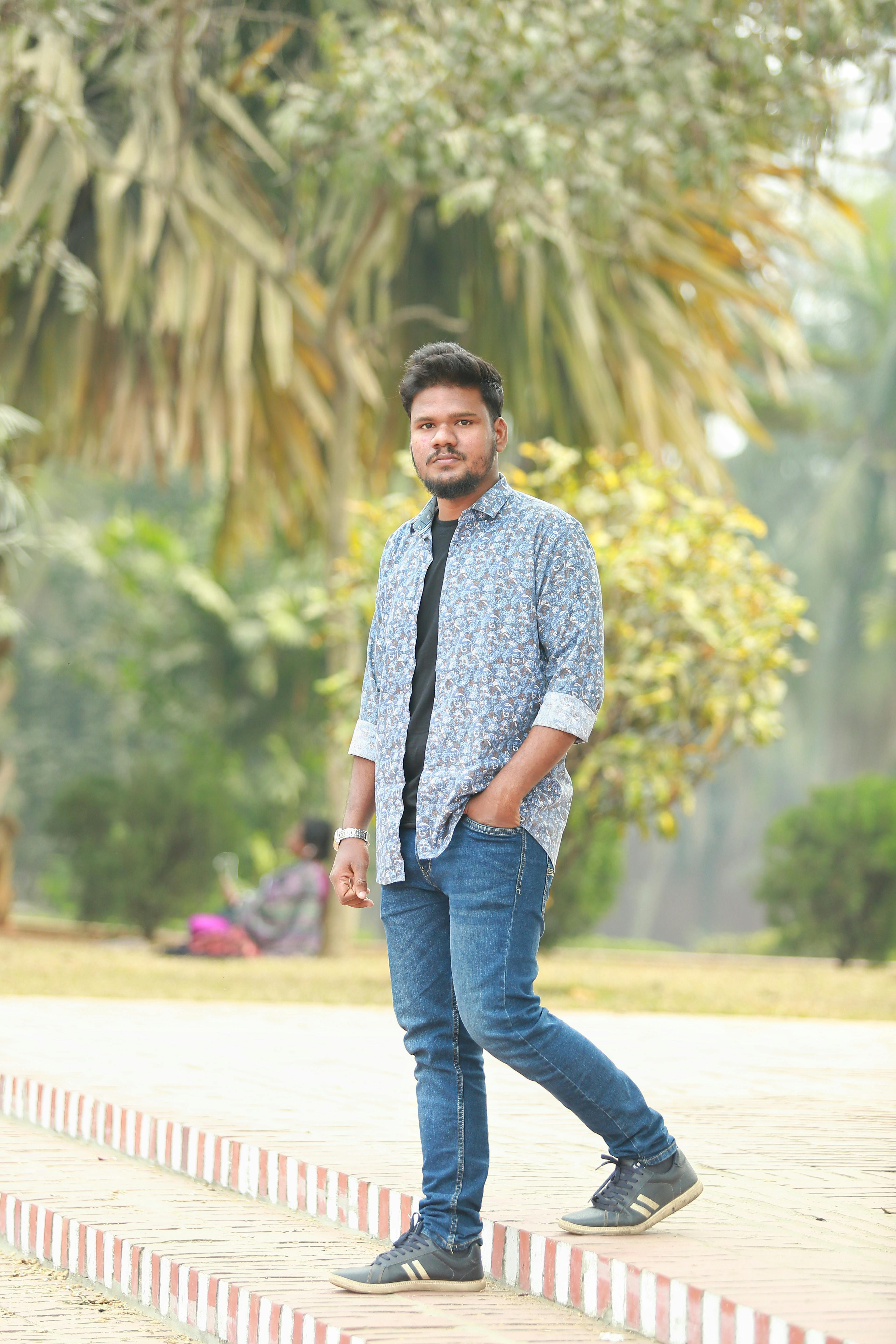 A young man in casual attire poses confidently outdoors on a sunny day.