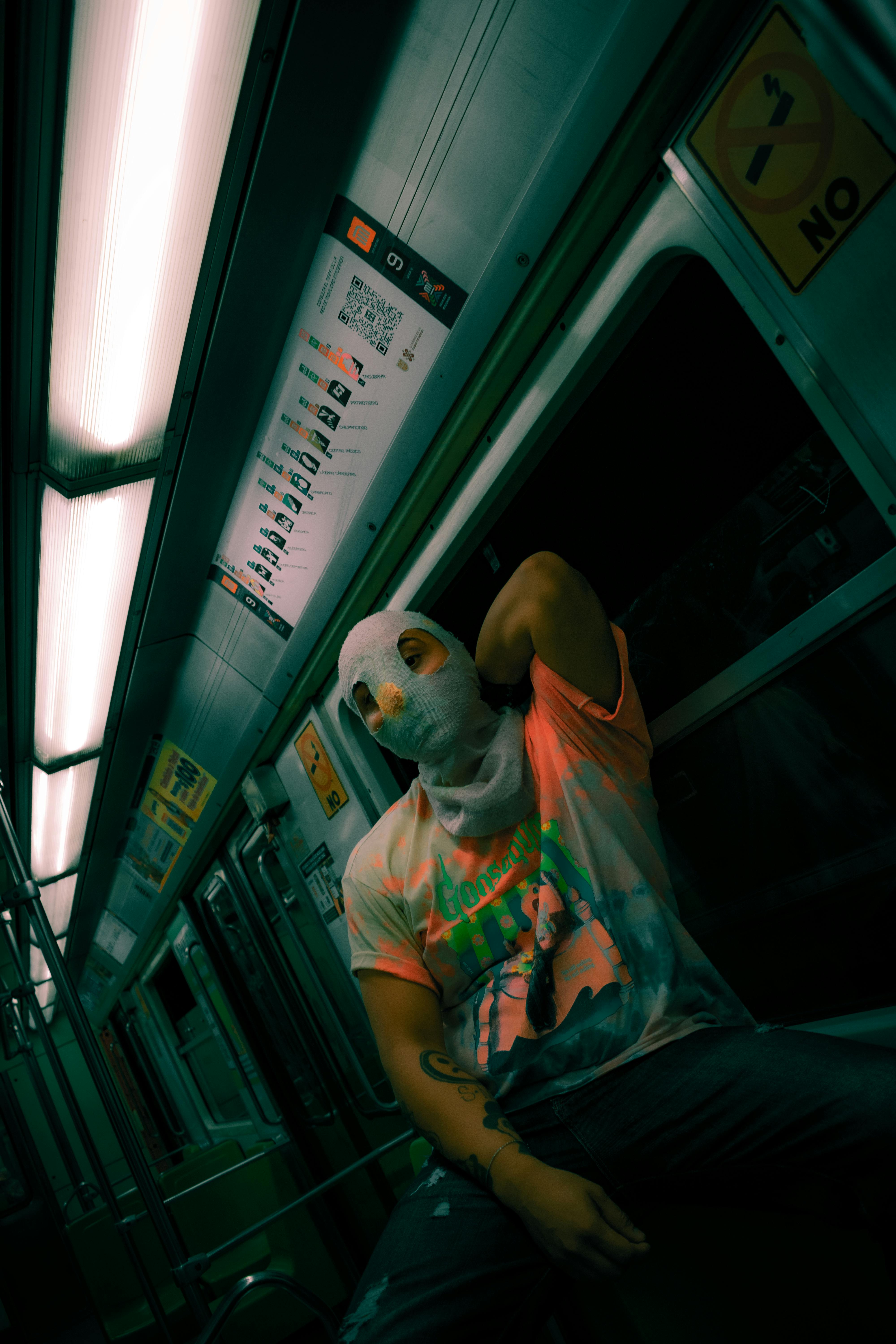 Free Person wearing mask sitting in dimly lit subway car, evokes mystery and urban exploration. Stock Photo
