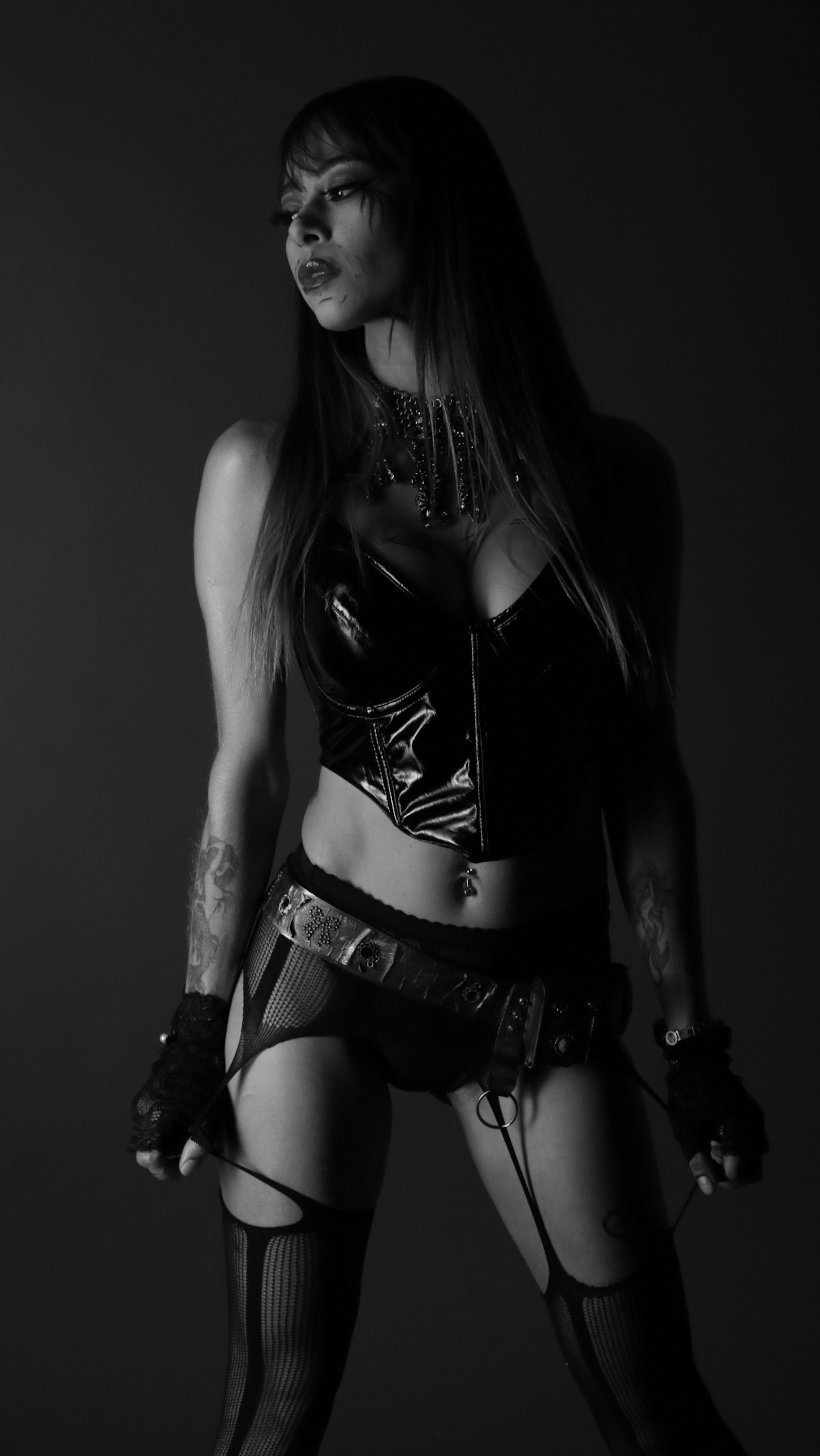 Moody black and white portrait of a woman in leather and fishnet fashion.