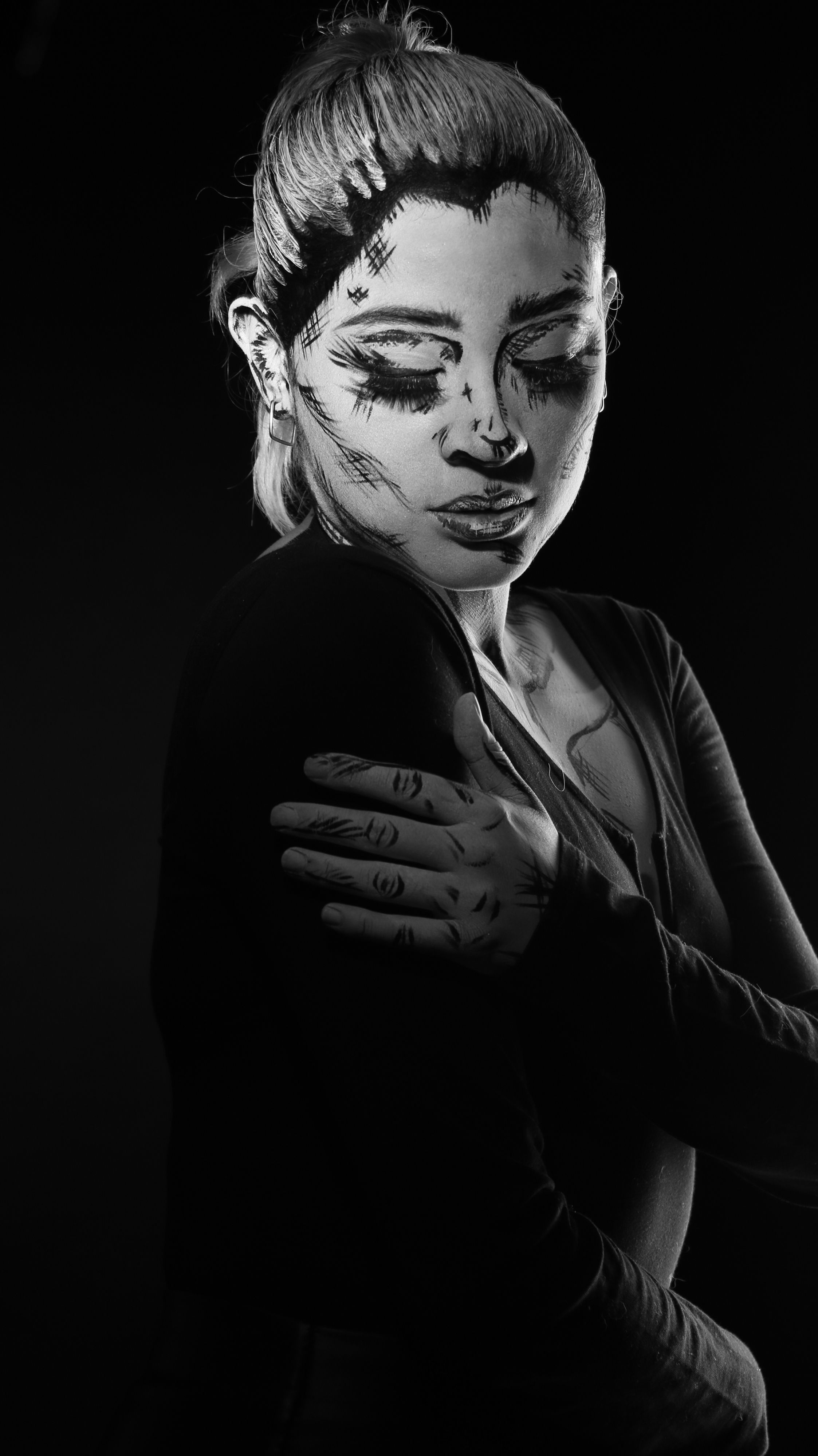 Black and white portrait of a woman with expressive face paint, embracing dramatic art style.
