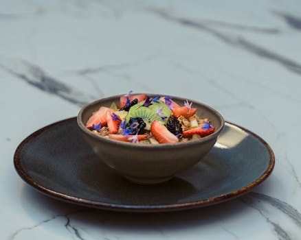 Delicious breakfast bowl featuring fresh fruits, granola, and edible flowers on marble table.