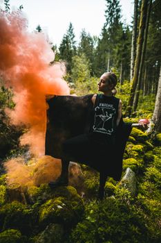 Woman in forest with red smoke bomb and mossy ground, creating a dramatic scene.