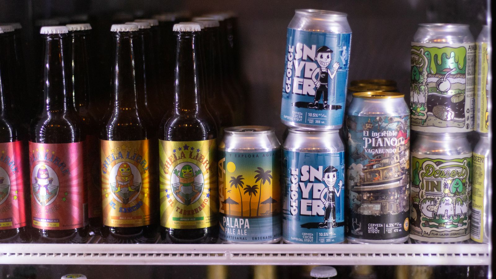 A selection of craft beer bottles and cans displayed in a refrigerator, showcasing unique branding.