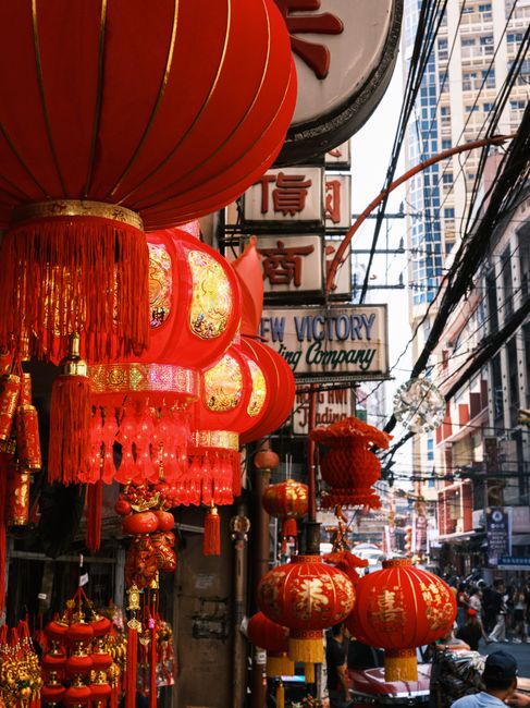 Colorful red lanterns decorate a bustling street filled with cultural signs and high-rise buildings.
