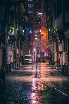 A colorful alleyway at night with rain creating reflections on the ground.