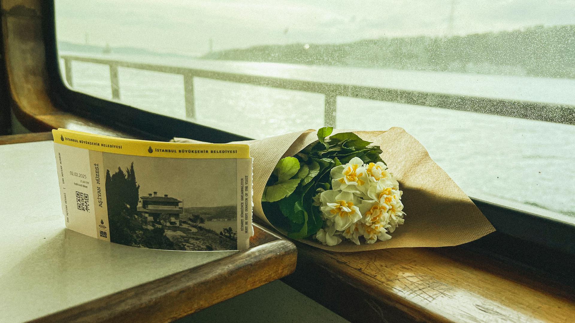 A bouquet of flowers and ferry tickets on a window seat with a view of Istanbul's waters.