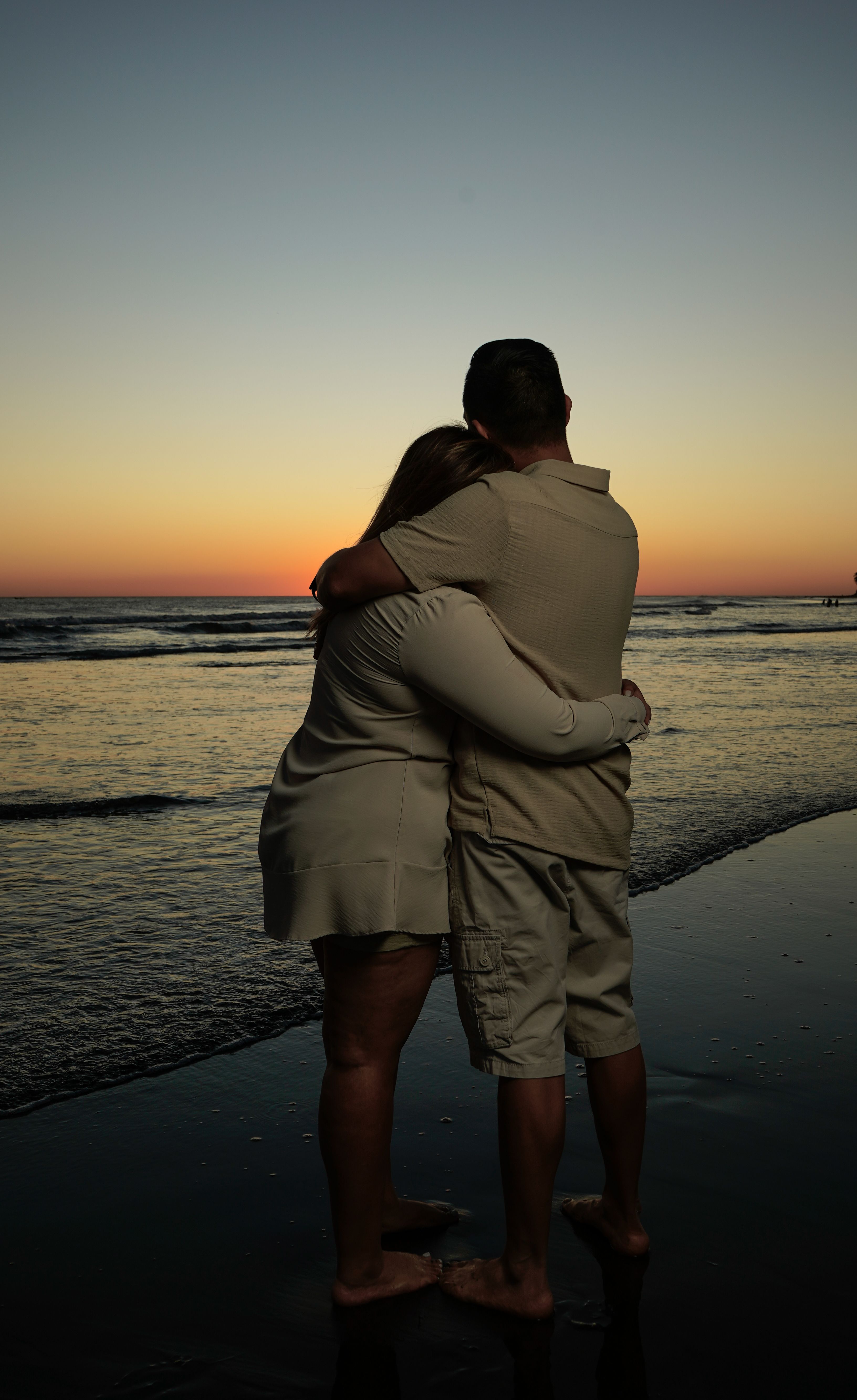 Gratis Una coppia si abbraccia su una spiaggia al tramonto, creando un'atmosfera romantica e serena. Foto a disposizione