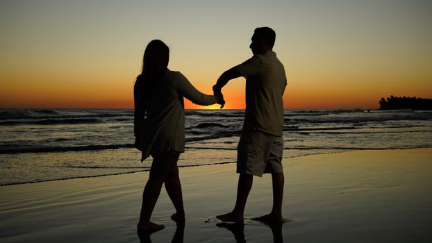 Couple dancing on the beach at sunset, creating a romantic silhouette scene.