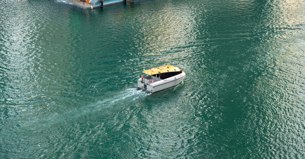 Aerial shot of a water taxi navigating through the calm, green waters of Dubai Marina.