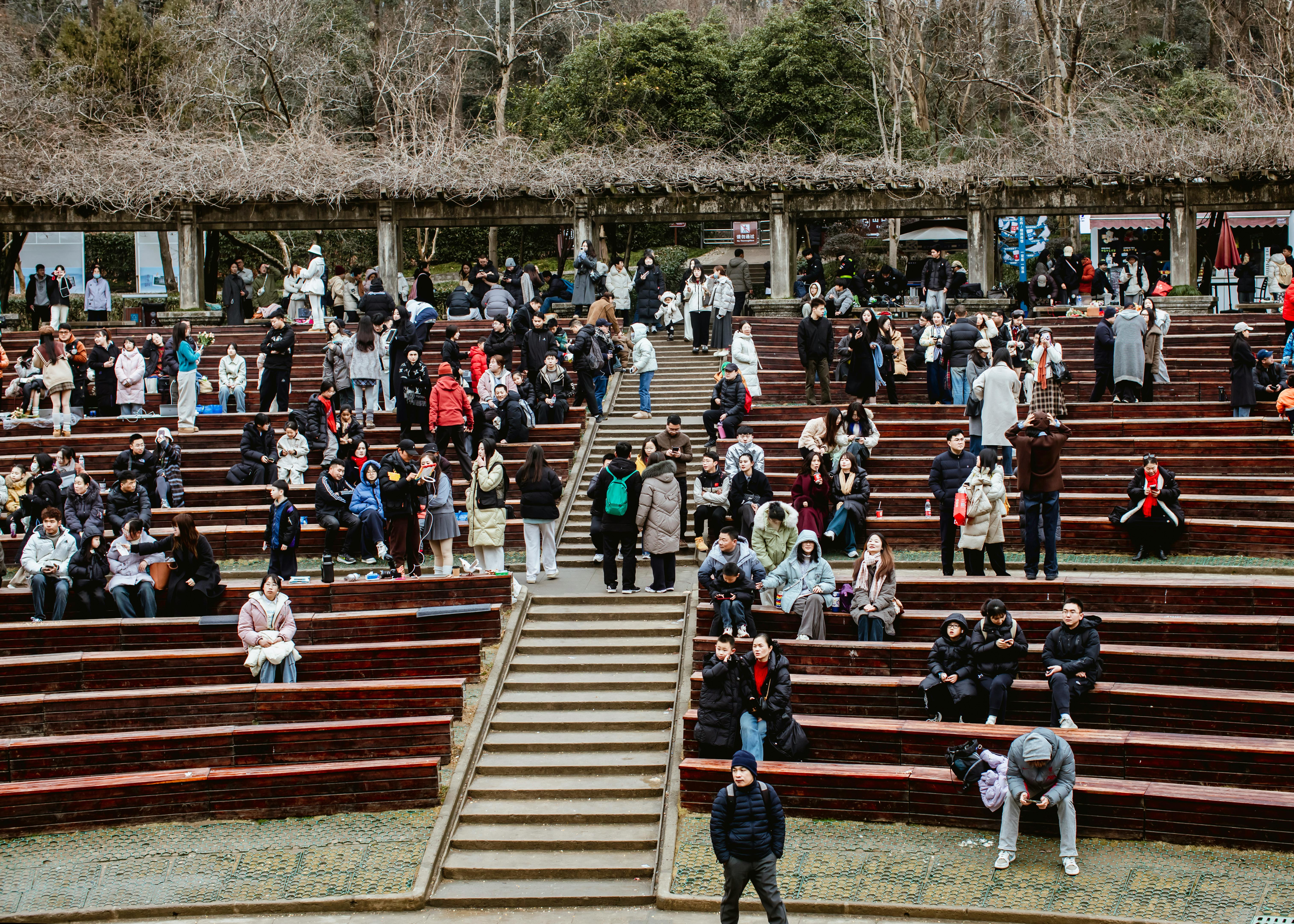 Crowd of people socializing at outdoor wooden amphitheater on a cool day.