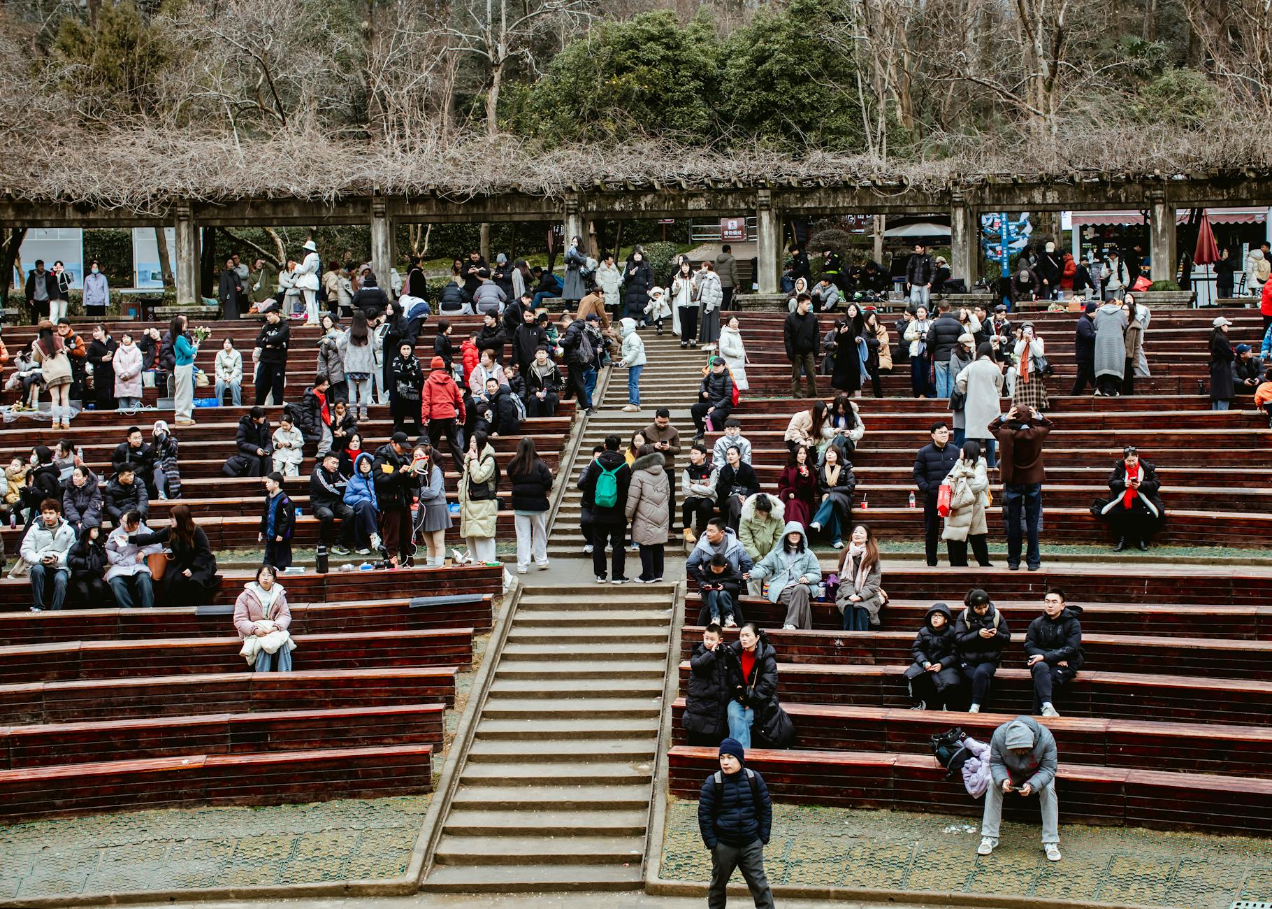 Crowd of people socializing at outdoor wooden amphitheater on a cool day.
