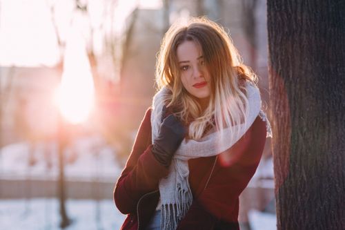 Free A woman in a cozy scarf enjoying a winter day with sunlight streaming through the trees. Stock Photo